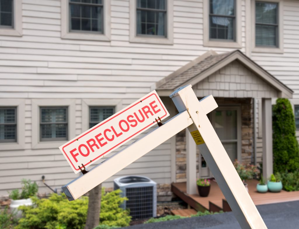 Close-up of a wooden "FORECLOSURE" sign in the front yard of a suburban house.
