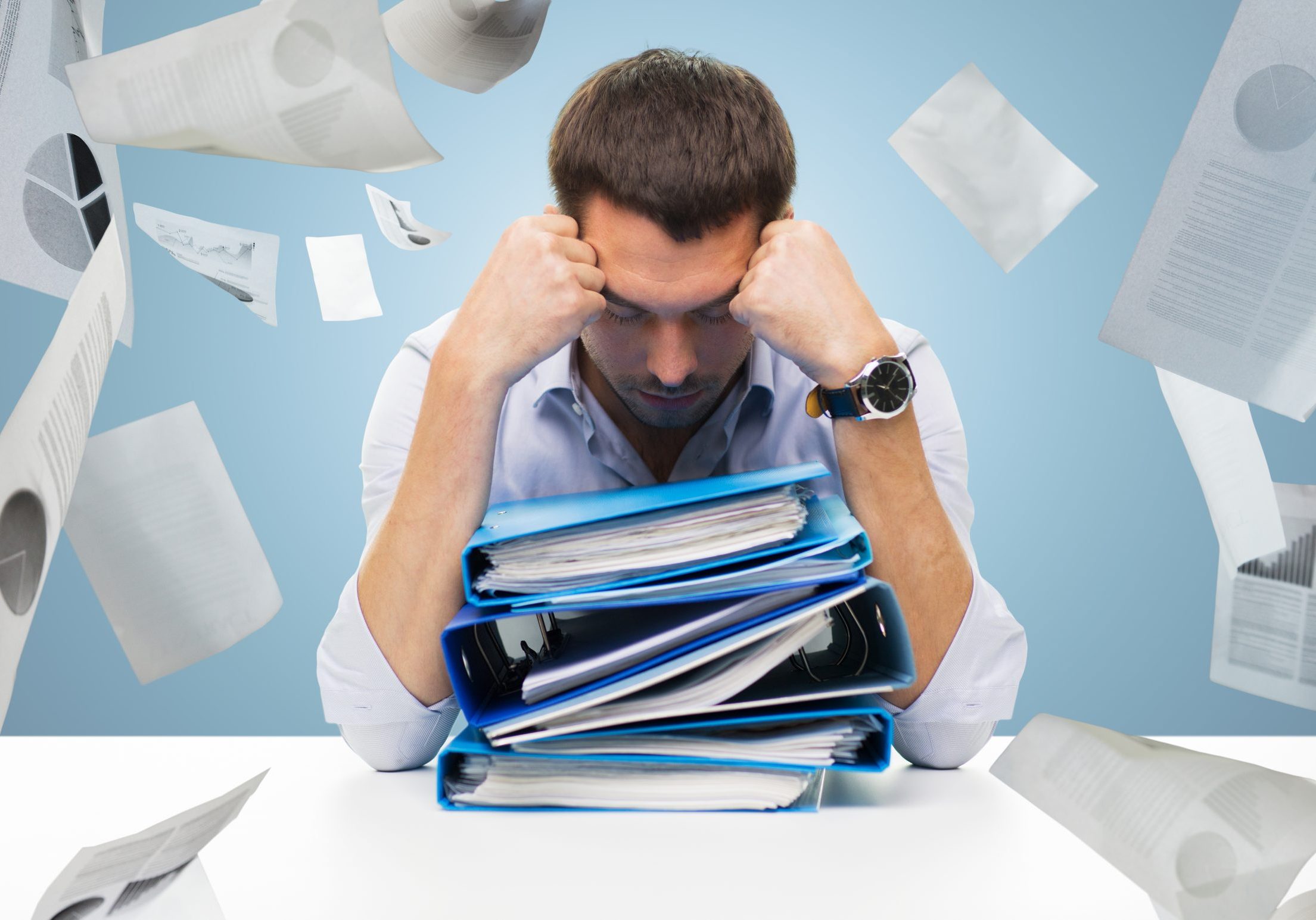 business, people, deadline, stress and paperwork concept - sad businessman with stack of folders and falling papers over blue background